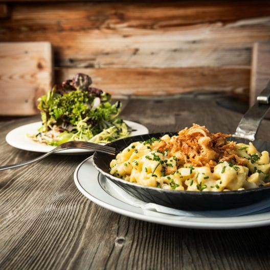 Pfanne mit Kasnockn und Salat auf Holztisch